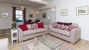Una sala de estar con dos sofás, una mesa de centro de vidrio, un jarrón con flores y un comedor con sillas y una mesa.