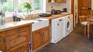 Une cuisine équipée d’un lave-linge intégré, de meubles en bois, d’une fenêtre donnant sur un espace verdoyant et d’un coin repas avec une table et des chaises en bois.