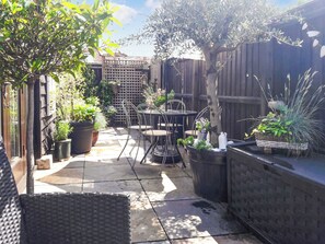 A patio area with a table and chairs, surrounded by potted plants and a wooden fence.
