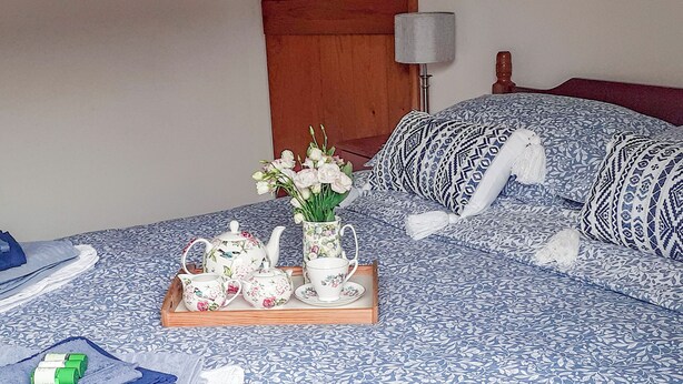 A neatly made bed with a floral-patterned bedspread, a tray with tea set and flowers, and a wooden headboard. - This is the ideal base for discovering and exploring Dorset. (East Burton, near Wool)