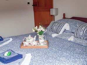 Ein ordentlich bezogenes Bett mit einer blumigen Tagesdecke, ein Tablett mit Teeservice und Blumen, und ein Holzkopfstück.