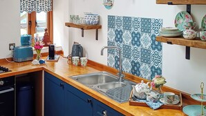 A kitchen with a wooden countertop, a sink, and blue cabinets. There are decorative items on the counter and a window with curtains. - This is the ideal base for discovering and exploring Dorset. (East Burton, near Wool)