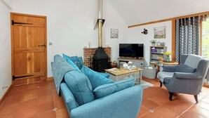 A living room with a sofa, armchair, TV, fireplace, and a bookshelf. - This is the ideal base for discovering and exploring Dorset. (East Burton, near Wool)