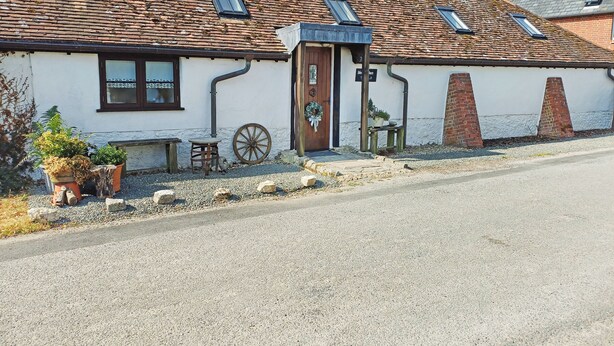 A traditional building with a sloped roof, a wooden door, and a small outdoor seating area with a table and chairs. - This is the ideal base for discovering and exploring Dorset. (East Burton, near Wool)