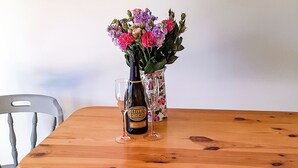 A wooden table with a bottle of Bella Cucina Prosecco and a vase of flowers. - This is the ideal base for discovering and exploring Dorset. (East Burton, near Wool)