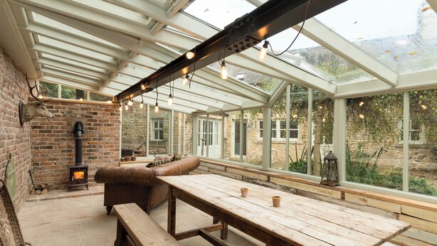 A conservatory with a wooden table and benches, a stone fireplace, and a view of the garden. - 3 bedroom accommodation in Riding Mill, near Corbridge (Riding Mill, near Corbridge)