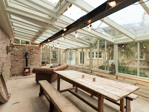 A conservatory with a wooden table and benches, a stone fireplace, and a view of the garden.