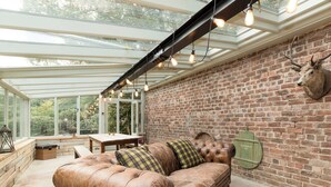A conservatory with a brick wall, a leather sofa, and a mounted deer head. - 3 bedroom accommodation in Riding Mill, near Corbridge (Riding Mill, near Corbridge)