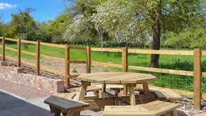 A picnic area with wooden tables and benches, surrounded by a wooden fence and a grassy field. - 4 bedroom accommodation in Ashperton, near Ledbury (Ashperton, near Ledbury)