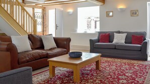 A living room with a brown leather sofa, a grey sofa, a wooden coffee table, and a red patterned rug. - 4 bedroom accommodation in Ashperton, near Ledbury (Ashperton, near Ledbury)