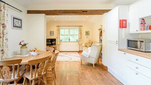 A cozy kitchen with wooden flooring, a dining area with a wooden table and chairs, a television, and a window with curtains. - COTTAGE IN THE POND W43212 (Garton, near Hornsea)