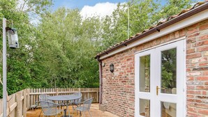 A patio with a table and chairs, a wooden fence, and a brick building with a white door. - COTTAGE IN THE POND W43212 (Garton, near Hornsea)