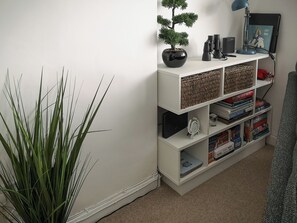 A white bookshelf with a bonsai tree, a lamp, and various books. - Seascape - St Catherine's Court (Fowey)