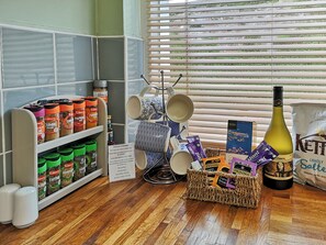A kitchen area with shelves of spices, a coffee maker, a wine bottle, and a basket of snacks.