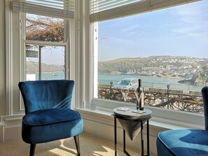 A room with a large window, a blue chair, and a small table with a bottle and glasses. - Seascape - St Catherine's Court (Fowey)