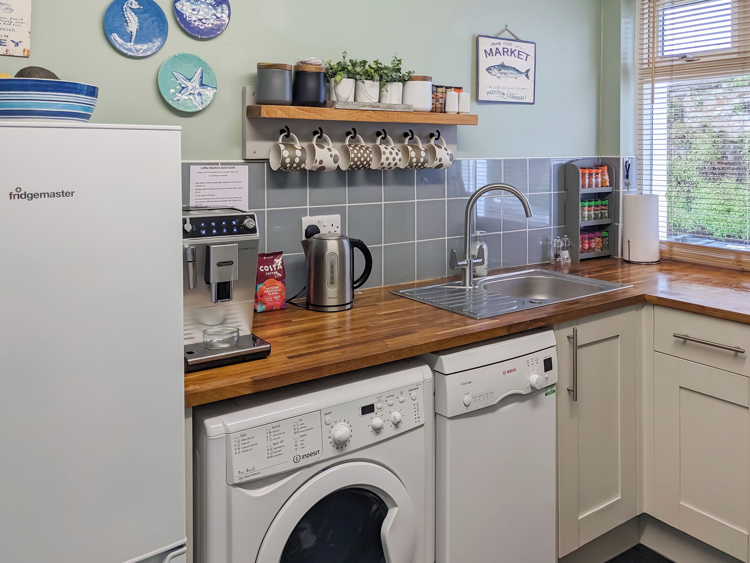 A kitchen with a Bosch dishwasher, a coffee machine, a sink, and a window with blinds.