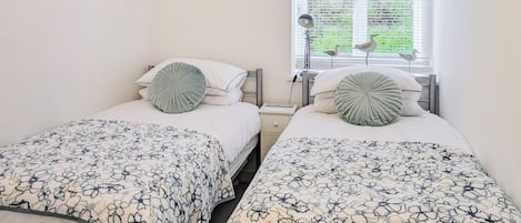 Habitación doble con dos camas, cada una con una colcha estampada de flores, una lámpara de noche y una ventana con persianas.