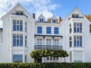 Un grand bâtiment blanc, à plusieurs étages, doté d’une façade symétrique, de nombreuses fenêtres et d’un balcon central orné de ferronnerie ouvragée.