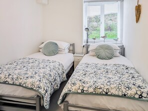Une chambre à deux lits, chacun étant agrémenté d’une couvre-lit à motifs floraux, d’une lampe de chevet et d’une fenêtre avec des stores.