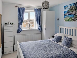 Une chambre à coucher avec un lit, une commode, un radiateur, une fenêtre avec des rideaux et un tableau accroché au mur.
