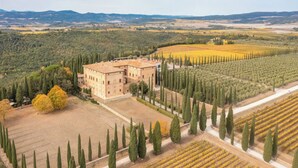 An aerial view of a large building surrounded by fields and cypress trees.