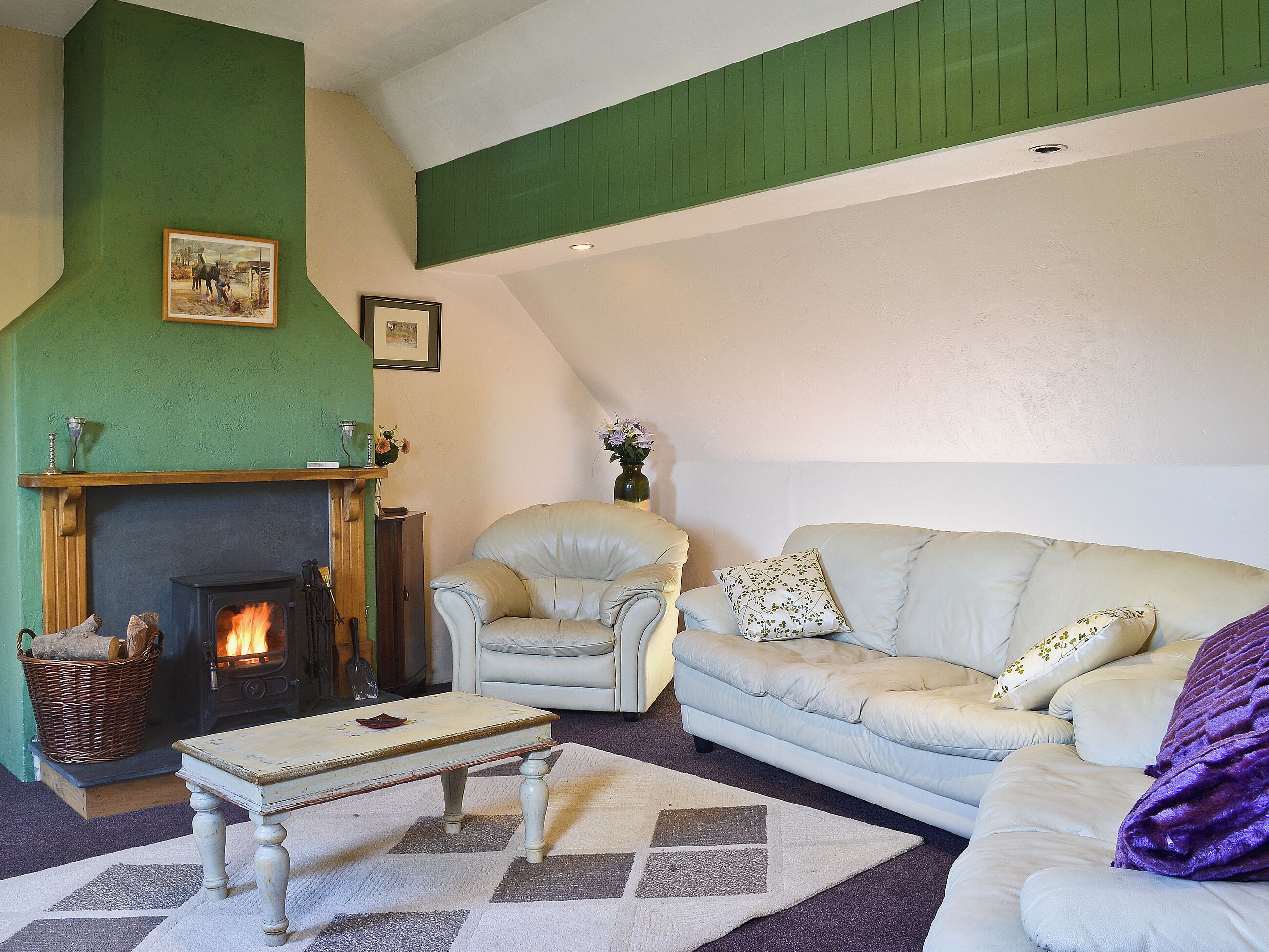 A cozy living room with a fireplace, a green accent wall, a white sofa, and a patterned rug.