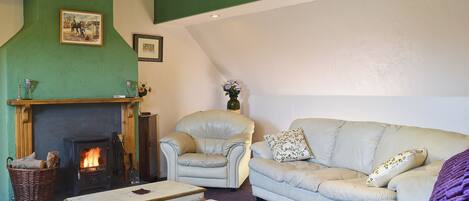 A cozy living room with a fireplace, a green accent wall, a white sofa, and a patterned rug.