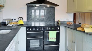 A kitchen with a black stove, a yellow kettle, and a sink.