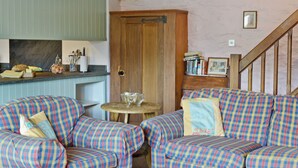 A cozy room with a checkered sofa set, a wooden door, and a kitchen area with a counter and various items.