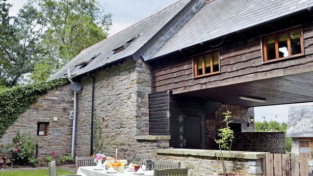 A rustic stone building with a wooden table set for dining, surrounded by a well-maintained garden.