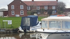 Twee boten aanmeren in een gracht, met een huis op de achtergrond.