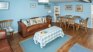 Een gezellige woonkamer met een bruine leren bank, een blauw-wit geruit tafeltje en houten stoelen.