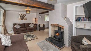 A cozy living room with a fireplace, brown sofas, a patterned rug, and a bookshelf.