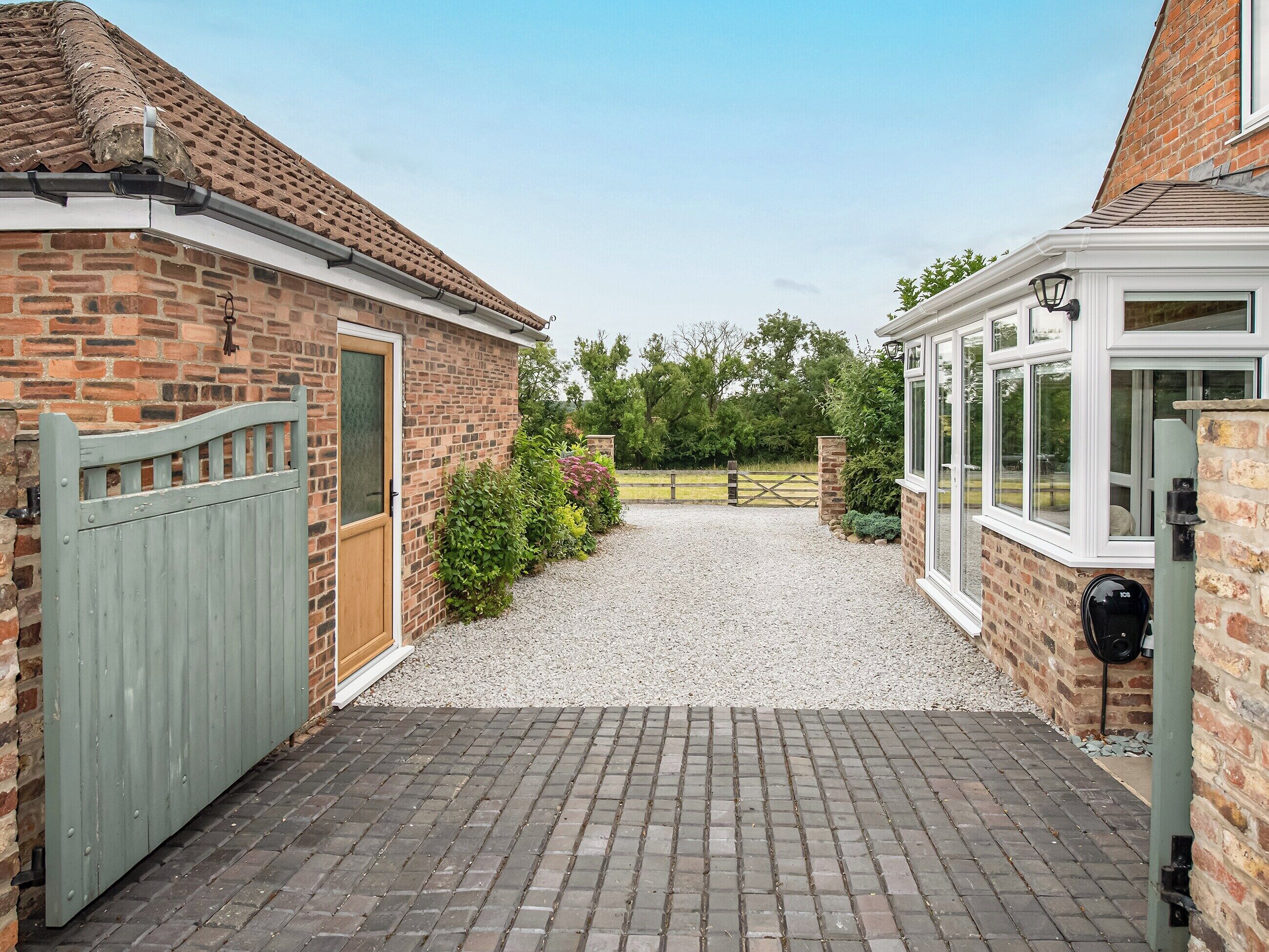 A brick house with a gravel driveway leading to a gated entrance.