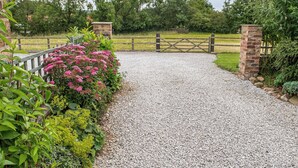 A gravel driveway leading to a gated entrance with a brick pillar and a wooden fence.