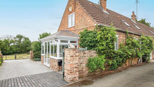 A brick house with a conservatory, a stone wall, and a gravel driveway.