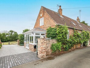 A brick house with a conservatory, a stone wall, and a gravel driveway.