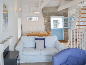 A cozy living room with a light blue sofa, a blue armchair, and a dining area with a wooden table set for a meal. - Beach Corner Cottage (Gorran Haven, near St Austell)
