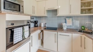 Uma cozinha moderna com armários brancos, micro-ondas, forno, cafeteira e chaleira.