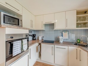 A modern kitchen with white cabinets, a microwave, an oven, a coffee maker, and a kettle.