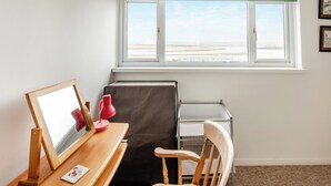 Quarto com escrivaninha, cadeira e janela com vista para a praia.