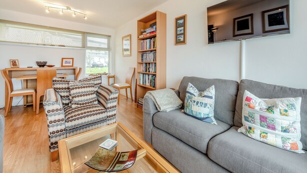 A modern living room with a grey sofa, patterned cushions, a coffee table, and a bookshelf.