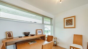 A dining area with a wooden table, chairs, a framed picture, and a window with blinds.