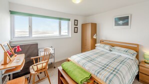 Um quarto com cama, escrivaninha, cadeira, guarda-roupa e janela com vista.
