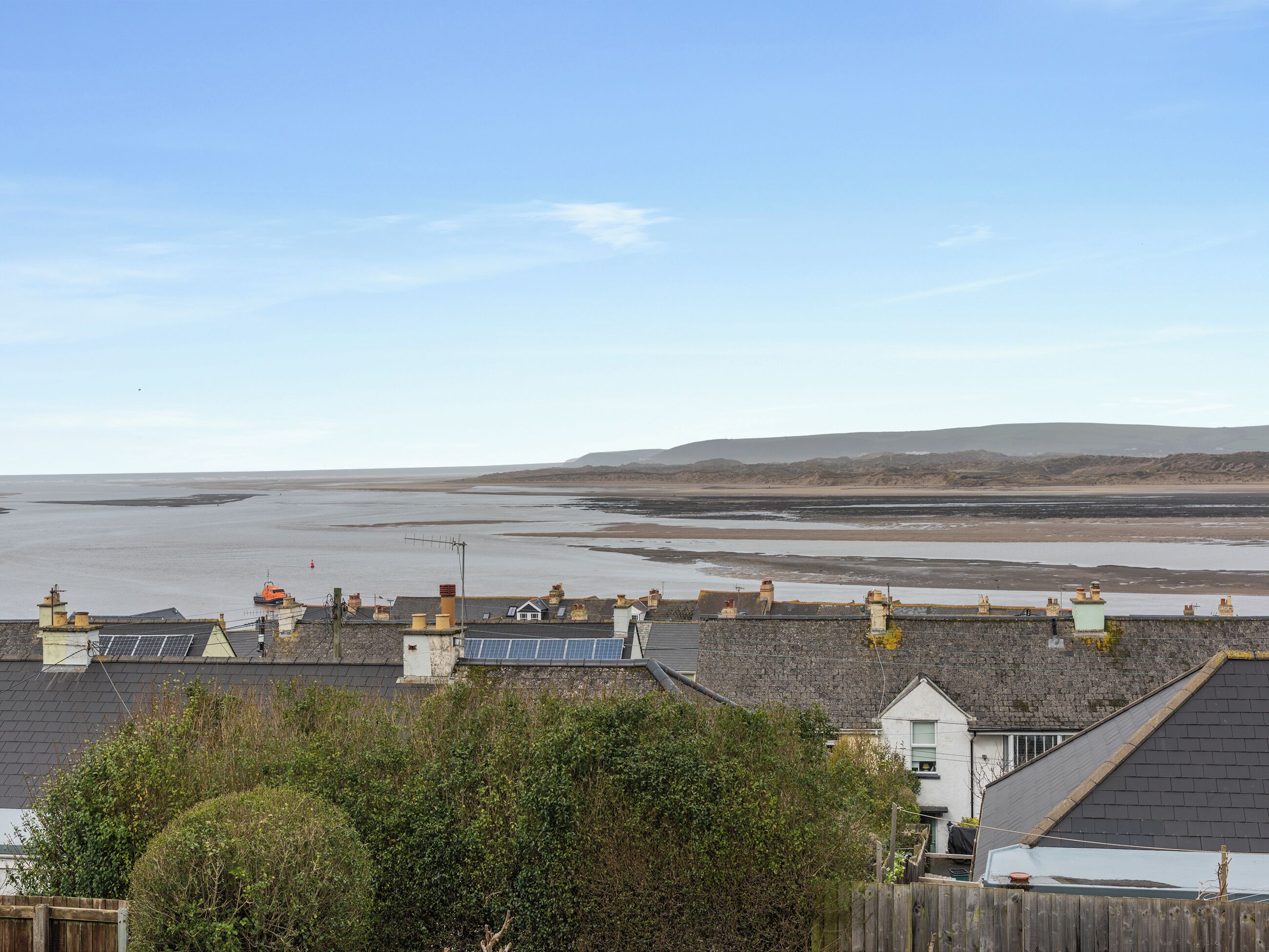 A coastal residential area with houses, a beach, and hills in the distance.