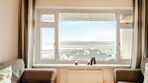 A room with a large window, two sofas, a radiator, and a view of a coastal landscape.