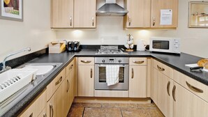 Una cocina compacta con armarios de madera, estufa de acero inoxidable, microondas y pileta.