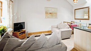 Una sala de estar con televisor, sofá, una mesa de comedor con sillas y una zona de cocina.