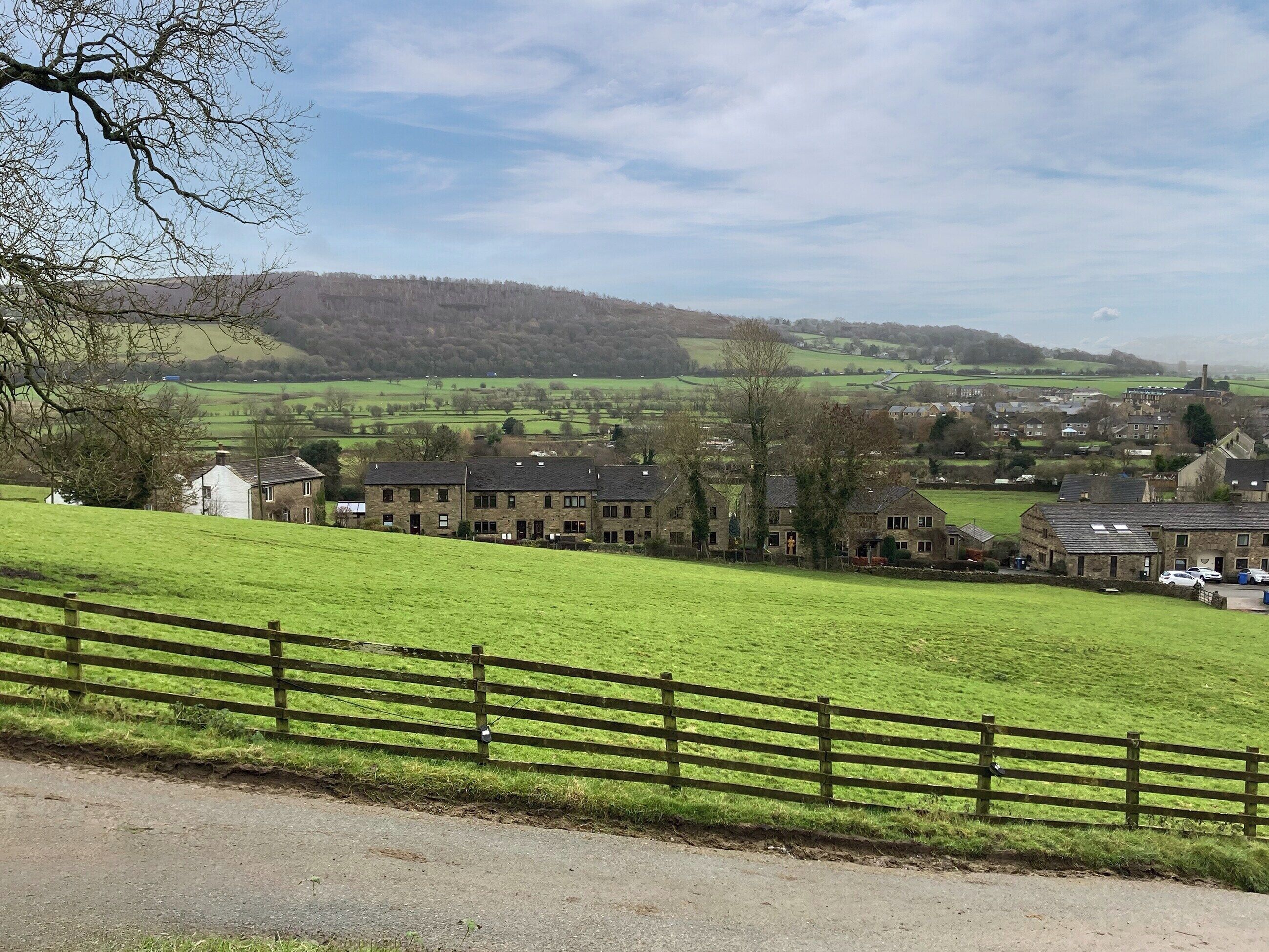 A rural village with stone buildings, a grassy field, and a wooden fence.