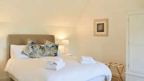 A neatly made bed with floral pillows, a bedside lamp, and folded towels. - No. 1 The Old School (Puddletown, near Dorchester)